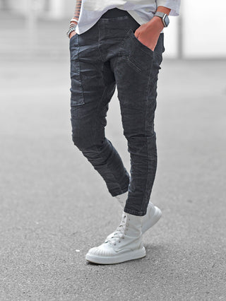 Person trägt OFF#DLY Joggpant Vellano black denim mit schlanker Passform und Patch-Taschen, kombiniert mit weißen High-Top-Sneakers. Ein legerer Street-Style-Look mit Armbändern und Smartwatch vervollständigt das Bild.