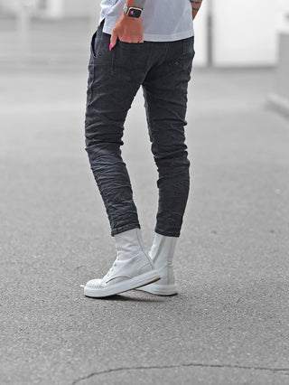 Eine Person trägt die OFF#DLY Joggpant Vellano black denim, kombiniert mit weißen High-Top-Sneakern. Die Hose bietet eine schlanke Passform mit einem Strickbund und Kordelzug für urbanen Komfort.