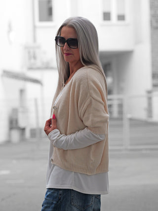 Frau mit silbernem Haar trägt den BSB Cardigan Ivoire. Der gestrickte Kurzarm-Cardigan in gedecktem Pink hat Perlmuttknöpfe, kombiniert mit weißen Langarmshirt und blauen Jeans, verleiht er Eleganz.