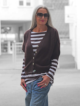 Frau auf Straße trägt BSB Cardigan chocolate: brauner Strick mit Perlmuttknöpfen, über Streifenshirt und Jeans, lässig-elegant gestylt. Graues Haar, schwarze Sonnenbrille, pinke Nägel, silberner Ring.