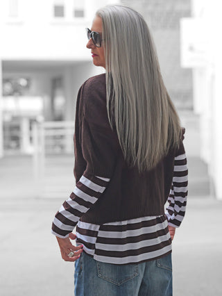 Person mit langem, silbernem Haar trägt BSB Cardigan chocolate mit kurzen Ärmeln und Perlmuttknöpfen über gestreiftem Top, kombiniert mit blauen Jeans.