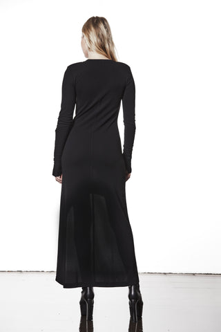 Rückansicht eines Models im Thom Krom Dress WD 52 black, bodenlang und figurbetont mit leicht ausgestelltem Rock. Dazu trägt sie schwarze, klobige Ankle Boots mit Absatz.