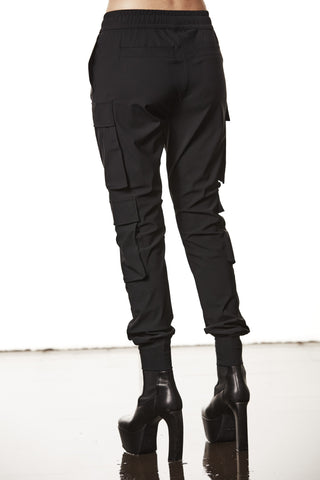 Thom Krom Pant WP 15 black: Slim Cargo-Hose mit Klappentaschen und elastischen Bündchen, kombiniert mit hohen schwarzen Plateau-Stiefeletten, präsentiert in einem minimalistischen Studio-Setting.