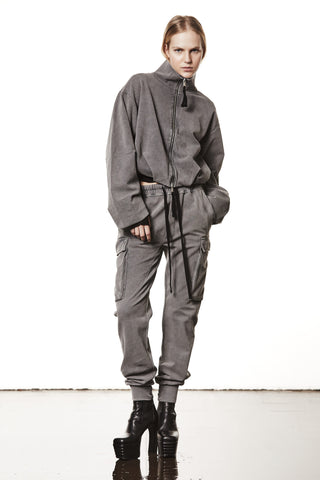 Person trägt die Thom Krom Jacket WSJ 494 used grey, eine oversized Jacke mit Stehkragen, Zweiwege-Reißverschluss und Tunnelzugsaum, kombiniert mit passenden Cargo-Joggern und schwarzen Plattformstiefeln.