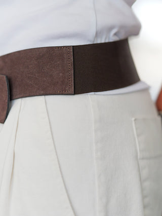 Nahaufnahme einer Taille mit einem BSB Belt brown one Size, der aus Wildleder und elastischem Material besteht, über einem hellcremen Rock oder Hose getragen und mit einem weißen Oberteil kombiniert wird.