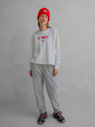 Person trägt Penn&Ink Sweater print ecru/tomato mit ST. MORITZ und rotem Stern vorne, kombiniert mit grauen Jogginghosen und schwarzen Trail-Sneakern.