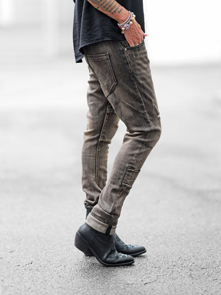Person in OFF#DLY Denim Cecina black Denim, zeigt markante Waschung und dezente Destroyed-Details. Slim-Fit-Stil mit Teilungsnähten, ergänzt durch schwarze Lederstiefeletten und Armband.