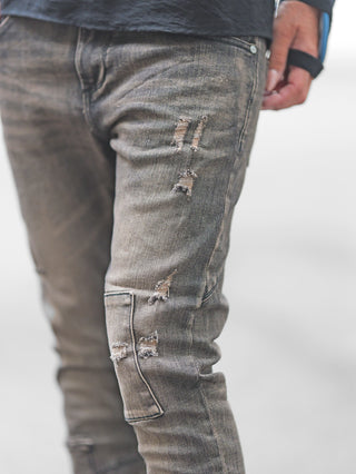 Nahaufnahme von einer Person, die die OFF#DLY Denim Cecina black Denim trägt: Slim-Fit, ausgebleicht, mit dezenten Rissen und fransigen Details an Schenkel und Knie, betont den urbanen, individuellen Stil.