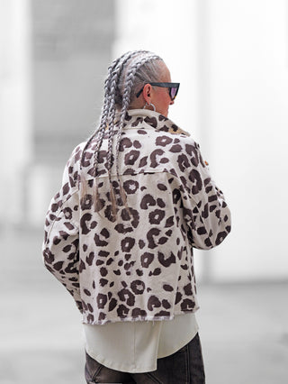Person mit langen, silbernen Zöpfen trägt die OFF#DLY Jacke Sirmione beige brown mit auffälligem Leopardenmuster, fransigem Saum und dunkler Sonnenbrille. Darunter blitzt ein weißes Shirt hervor.