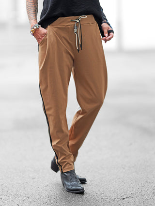 OFF#DLY Pamt Turin camel: Locker sitzende camelbraune Hose mit schwarzem Seitenstreifen, elastischem Bund und Seitentaschen, getragen mit schwarzen Stiefeletten. Ein sportlich-schicker Look für vielseitige Anlässe.