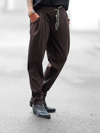 Person trägt OFF#DLY Pamt Turin brown, eine trendige Hose mit leicht konischem Bein und elastischem Bund. Kombiniert mit schwarzen Stiefeletten und bunten Armbändern, zeigt der Look sportlichen Chic.