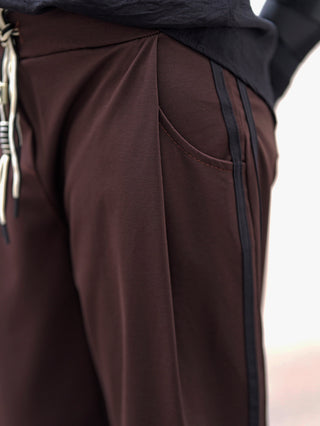 Nahaufnahme der OFF#DLY Pamt Turin brown: brauner Stoff mit plissiertem Bund, geschwungener Tasche, schwarzem Seitenstreifen, Kordeln am Bund und sichtbarem Saum eines dunklen Oberteils oben im Bild.