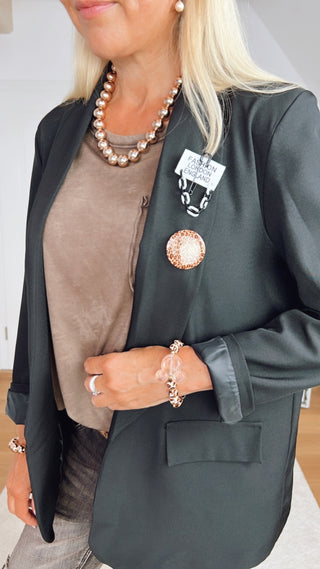 Nahaufnahme eines Outfits mit dem OFF#DLY Shirt Valentina schoko in Oversize-Schnitt, getragen unter einem dunklen Blazer, ergänzt durch eine metallische Perlenkette, Armbänder und dekorative Broschen.