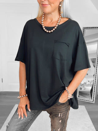 Person trägt das OFF#DLY Shirt Valentina black, ein oversized schwarzes T-Shirt mit Brusttasche, kombiniert mit distressed Jeans und metallischen Accessoires.