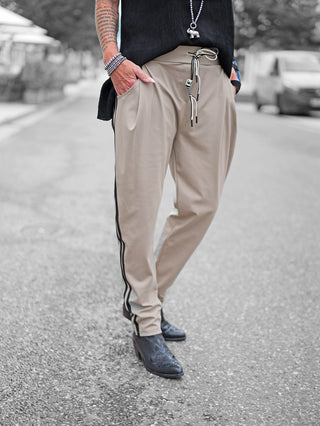 OFF#DLY Pant Turin taupe: Locker sitzende, taupefarbene Jogginghose mit schwarzen Seitenstreifen und Kontrastkordel, kombiniert mit schwarzen, spitz zulaufenden Stiefeletten für einen sportlich-eleganten Look.