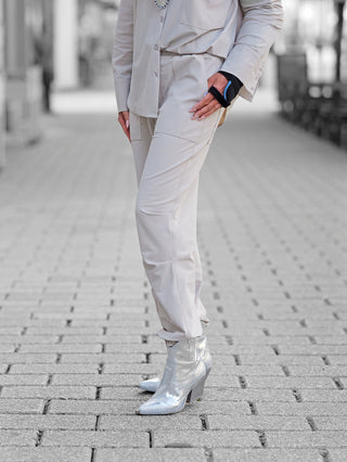 Person trägt Penn&Ink Trousers sand auf gepflastertem Weg; ein lässiger, eleganter Look mit elastischem Bund und Taschen. Kombiniert mit silbernen Stiefeletten und einem schwarzen Handgelenkstütze.