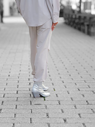 Penn&Ink Trousers sand: Locker geschnittene, hellbeige Hose mit elastischem Bund und Tunnelzug, getragen auf einem gepflasterten Platz, kombiniert mit silbernen, metallischen Cowboy-Stiefeletten.