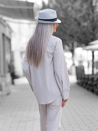 Eine Person trägt die Penn & Ink Bluse sand, eine oversize, minimalistische Bluse mit auffälliger Brusttasche, weiten Ärmeln und verlängertem Rücken, ideal für modernen, lässigen Stil.