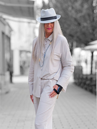 Person trägt die Penn & Ink Bluse sand in einem übergroßen Schnitt mit Statement-Tasche und weiten Ärmeln, kombiniert mit passender Hose und fedora.
