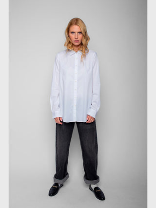 Person trägt Emily Bluse 4890-157120 white, langärmlig mit einfachem Kragen, kombiniert mit locker sitzenden, dunklen Jeans und schwarzen Loafers. Bluse hat Rüschen an den Ärmeln.