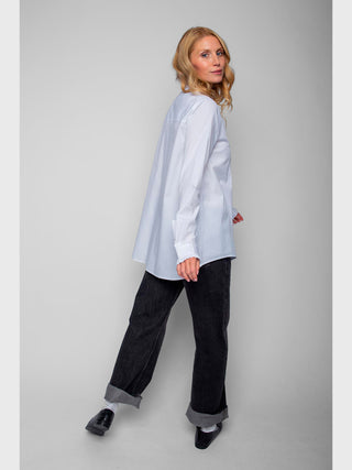 Frau trägt Emily Bluse 4890-157120 weiß, locker geschnitten mit Hemdblusenkragen und subtilen Rüschen an den Manschetten, kombiniert mit dunklen Jeans und schwarzen Slip-Ons, für einen minimalistischen Look.