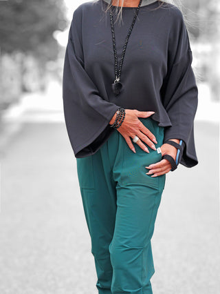 Die Aufnahme zeigt den BSB Pulli black, einen locker sitzenden, langärmligen Pulli mit weiten Ärmeln, getragen mit Accessoires und einem Handgelenkstützband, für einen urbanen, eleganten Look.