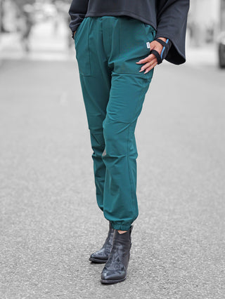 Eine Person trägt Penn&Ink Trousers forest, lässige Jogpants mit elastischen Bündchen, kombiniert mit schwarzen Lederstiefeletten. Die rechte Hand steckt in der Hosentasche.
