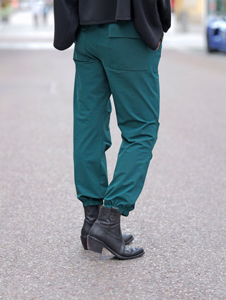 Person von hinten in Penn&Ink Trousers forest mit elastischen Bündchen und sportlichen Rippdetails, kombiniert mit schwarzen Lederstiefeletten. Die weichen Jogpants bieten lässigen Komfort und Stil auf der Straße.