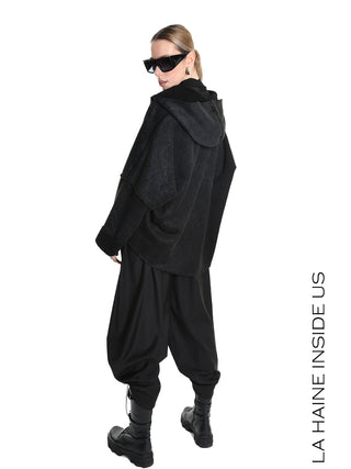 Modell in einem La Haine Jacket black W5168, einem übergroßen Kapuzenpullover, kombiniert mit weiten Haremshosen, klobigen Kampfstiefeln und eckigen Sonnenbrillen. Markenname LA HAINE INSIDE US am Bildrand sichtbar.