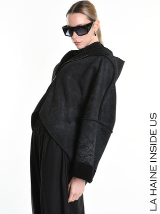 Model trägt La Haine Jacket black W5168, eine leicht verkürzte, shearling-gefütterte Kapuzenjacke mit versetztem Reißverschluss, kombiniert mit schwarzen, locker sitzenden Hosen, übergroßen, eckigen Sonnenbrillen und einfachen Tropfenohrringen.