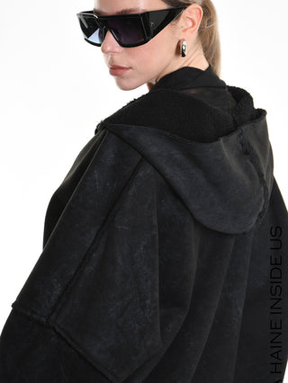 Frau trägt den La Haine Jacket black W5168, einen weit geschnittenen schwarzen Kapuzenmantel, kombiniert mit übergroßen eckigen Sonnenbrillen und klobigen Creolen in einem stilvollen Modeeditorial.
