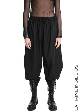 Modell präsentiert die La Haine Pant black LW5164: Haremhose mit elastischem Kordelzugbund, voluminösem Schnitt und verkürzter Länge. Kombiniert mit einem transparenten, taillierten Mesh-Top und klobigen Schnürstiefeln.
