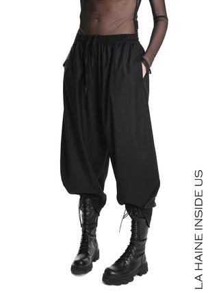 La Haine Pant black LW5164: Modells tragen lockere, tief sitzende schwarze Haremhose mit Seitentaschen und elastischem Bund. Kombiniert mit schwarzen Combat Boots, betont den urbanen, avantgardistischen Stil.