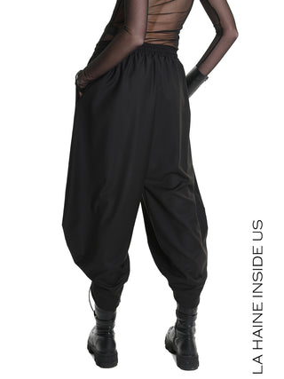 Modell trägt La Haine Pant black LW5164, lockere, verkürzte Haremhose mit elastischem Bund und Tunnelzug, kombiniert mit klobigen Stiefeln und transparentem Mesh-Top, markiert durch „LA HAINE INSIDE US“ Text rechts.