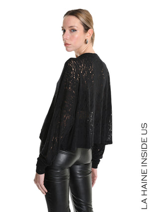 La Haine Sweater black LW5205: Model in einem locker sitzenden, schwarzen Spitzenpullover mit semitransparenter Struktur und langen Ärmeln, kombiniert mit eng anliegenden schwarzen Lederhosen und schlichten Creolen.