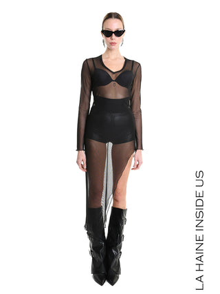 Model präsentiert das La Haine Dress black W5235: ein figurbetontes, transparentes Meshkleid mit asymmetrischem Saum und V-Ausschnitt, kombiniert mit schwarzen Lederstiefeln, Sonnenbrille und auffälligen Ohrringen.