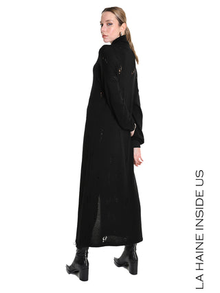 Junge Frau in La Haine Sweater LW5243 black, einem langen, leicht zerstörten Strickkleid mit hohem Kragen und Frontschlitz, posiert rückwärts, Kopf über Schulter, vor weißem Hintergrund.