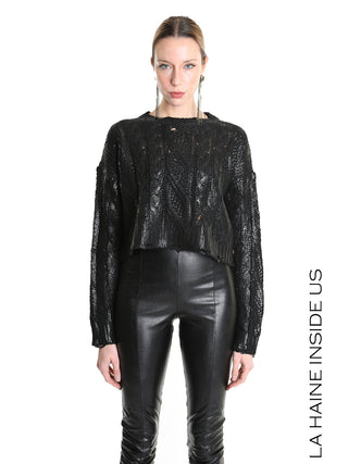 Eine Frau trägt den La Haine Sweater LW5136 black, einen locker gestrickten, leicht zerstörten schwarzen Pullover mit cropped Schnitt, kombiniert mit hochtaillierten, figurbetonten Lederhosen.