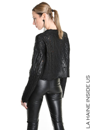 Frau trägt La Haine Sweater LW5136 black: kurzer, kastiger, schwarzer Zopfstrickpullover mit Glanzeffekt, kombiniert mit hochtaillierten schwarzen Leder-Leggings. Marke LA HAINE INSIDE US am rechten Rand sichtbar.