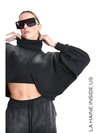 Model trägt La Haine Sweater LW5226 black, einen verkürzten, lockeren Sweater mit überkreuztem Saum und batwing-Ärmeln. Kombiniert mit oversized Sonnenbrille und passenden schwarzen Jogpants für urbanen Look.