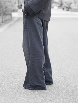 Gitta Banko Rylee W.Black: Weit ausgestellte, bodenlange Jeans mit hohem Bund und dezenten Bundfalten; aus elastischem Baumwollmix, kombiniert mit einer dunklen Jacke mit shearlingartigen Bündchen.
