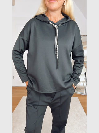 Person trägt das OFF#DLY Sweatshirt Life black: schwarzer Hoodie mit weißen Kordeln, lockerem Schnitt, Zitat-Patch am Ärmel. Kombiniert mit passenden schwarzen Jogger-Hosen, zeigt einen entspannten, urbanen Stil.