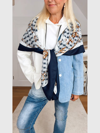 Erwachsene Frau trägt GUESS Noelle Scarf 130x130 BLU mit Kettengürtel-Print, locker um die Schultern drapiert, über weißem Hoodie und Jeansjacke, passend zu ihrem lässigen Outfit.