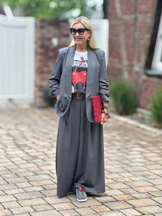 Person trägt den OFF#DLY Blazer Eleonora Grau: locker geschnitten, leicht tailliert mit gerafften 3/4-Ärmeln, kombiniert mit weißem T-Shirt und roter Clutch.