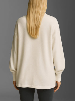 Eine Person trägt den Cotton Candy Cardigan Malea offwhite/mela, einen oversized Strickpullover mit Ballonärmeln und gerippten Bündchen, kombiniert mit dunklen, schmalen Hosen.