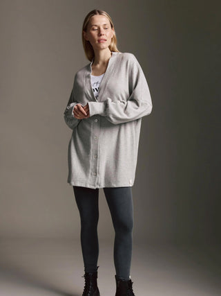 Frau trägt den Cotton Candy Cardigan Malea grey/melan, oversized mit Ballonärmeln, über einem weißen T-Shirt und dunklen Leggings, kombiniert mit schwarzen Stiefeletten.