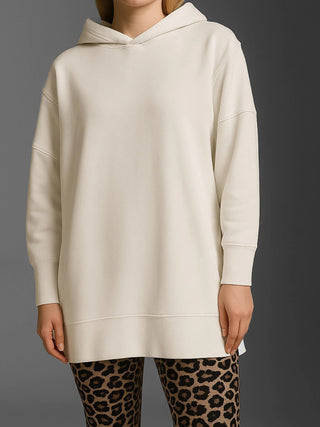 Person trägt das Cotton Candy Sweatshirt Luna offwhite, ein langes, oversized Kapuzen-Sweatshirt ohne sichtbare Grafiken, kombiniert mit Leopardenmuster-Leggings, vor grauem Hintergrund.
