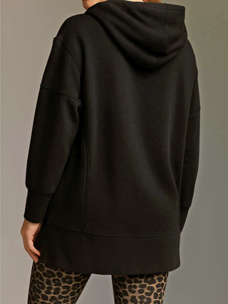 Person von hinten in einem oversized Cotton Candy Sweatshirt Luna black mit Kapuze und langen Ärmeln, kombiniert mit eng anliegenden Leopardenmuster-Leggings vor neutralem Hintergrund.