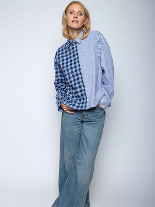 Person in oversized Emily Bluse 8645-157400, geteilt in blau-schwarz kariert und blau-weiß gestreift, kombiniert mit locker sitzenden Jeans. Flanell-Design mit durchgeknöpfter Front und überschnittenen Schultern.