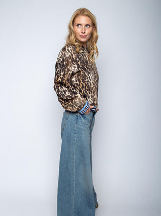 Frau im Profil trägt die Emily Bluse 8731-157512 Leo, eine locker sitzende, langärmelige Bluse mit Leopardenmuster, kombiniert mit hochtaillierten, weit geschnittenen Jeans.